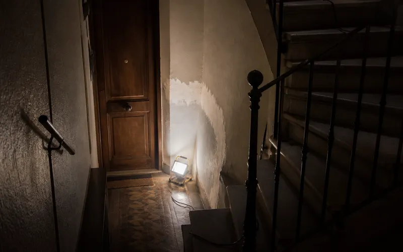 Rellano oscuro de Barcelona con lámpara portátil junto a la puerta, servicio urgente.
