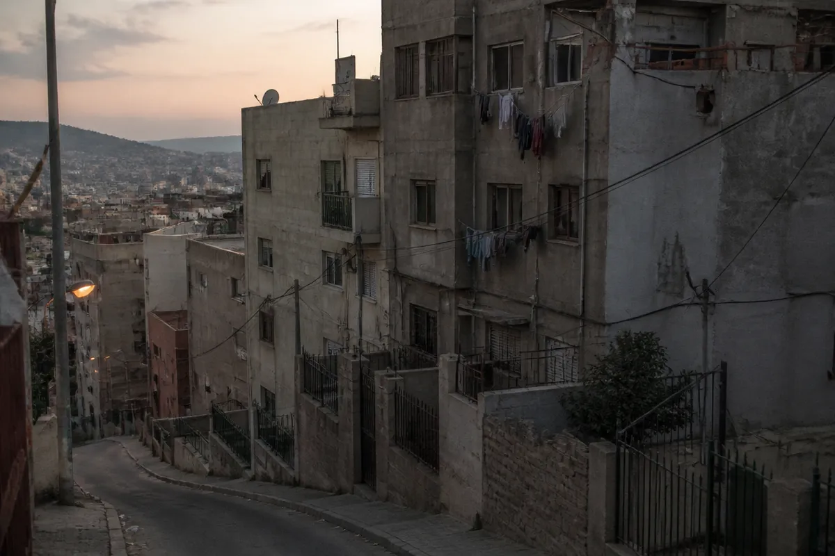 Ladera de comunidades altas con tendederos y hormigón visto, calle en pendiente vacía al atardecer.