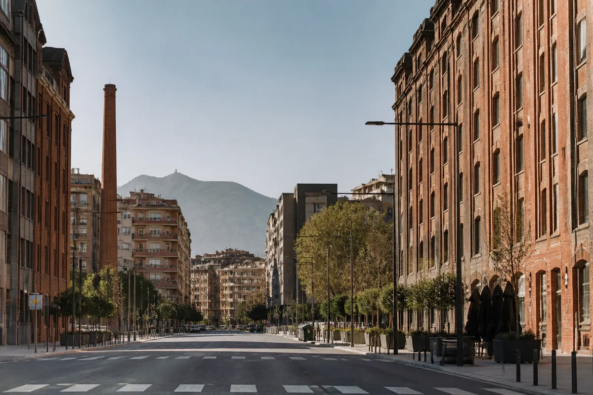 Ensanche interior con ladrillo industrial y una silueta de montaña al fondo, calle ancha sin tráfico ni marcas.